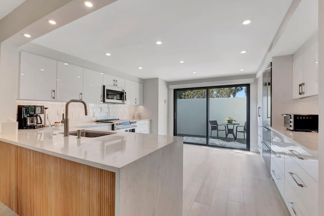 kitchen featuring sink, appliances with stainless steel finishes, kitchen peninsula, white cabinets, and backsplash