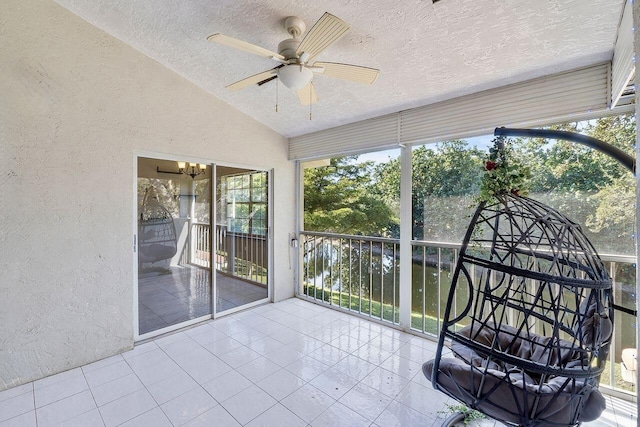 unfurnished sunroom featuring ceiling fan with notable chandelier, vaulted ceiling, and a water view