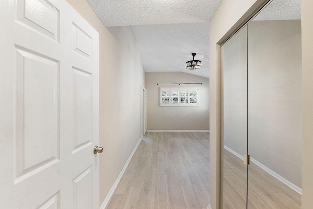 corridor featuring vaulted ceiling, a textured ceiling, and light hardwood / wood-style floors