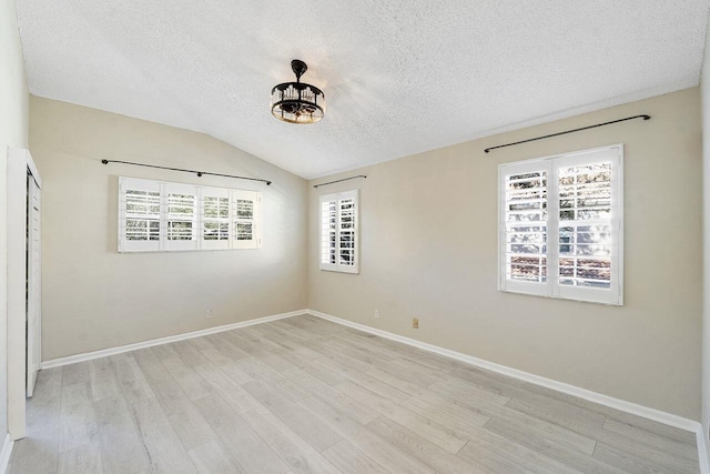 spare room featuring lofted ceiling, light hardwood / wood-style floors, and a textured ceiling