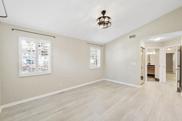 unfurnished room featuring vaulted ceiling, light hardwood / wood-style flooring, and a textured ceiling