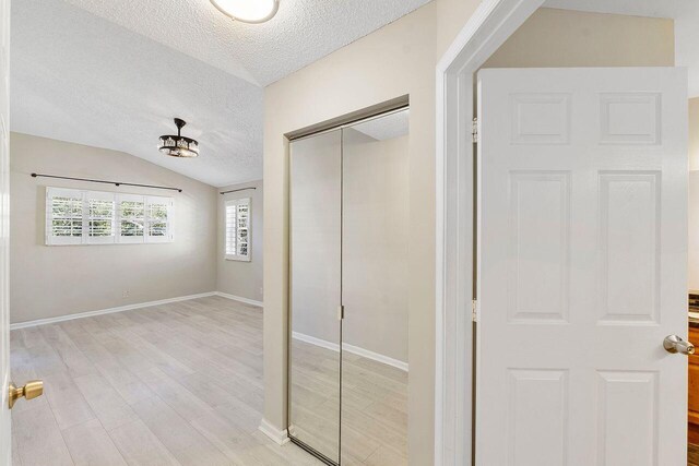 interior space featuring light hardwood / wood-style flooring, vaulted ceiling, and a textured ceiling