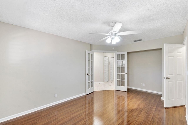 empty room featuring french doors, ceiling fan, dark hardwood / wood-style flooring, and a textured ceiling