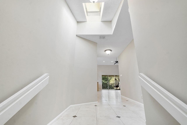 corridor featuring a textured ceiling, a high ceiling, and light tile patterned flooring