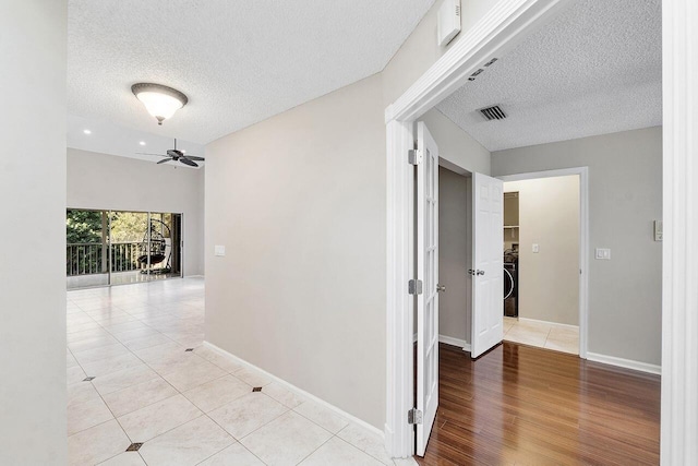 corridor featuring light tile patterned floors, washer / dryer, and a textured ceiling