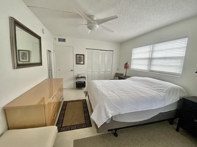 bedroom featuring ceiling fan, light tile patterned floors, a closet, and a textured ceiling