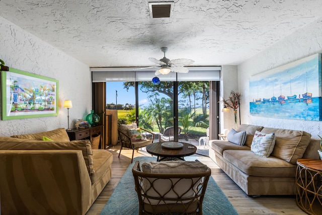 living room featuring ceiling fan, a wall of windows, wood-type flooring, and a textured ceiling