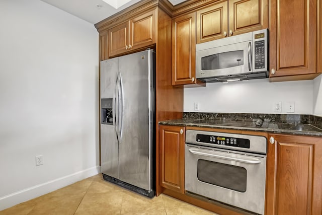 kitchen with stainless steel appliances, light tile patterned flooring, and dark stone countertops