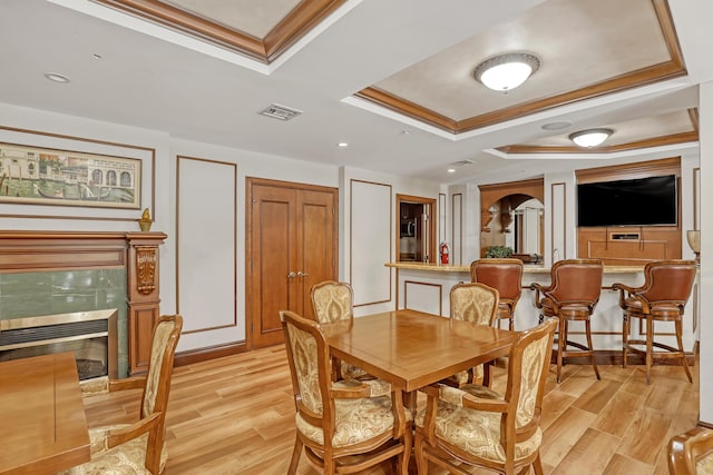 dining space featuring crown molding, a tray ceiling, light hardwood / wood-style flooring, and a tiled fireplace