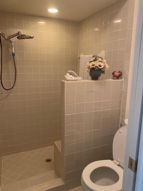 bathroom featuring a tile shower, tile walls, and toilet