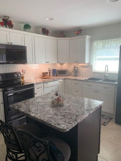 kitchen featuring white cabinetry, a breakfast bar, tasteful backsplash, and black appliances