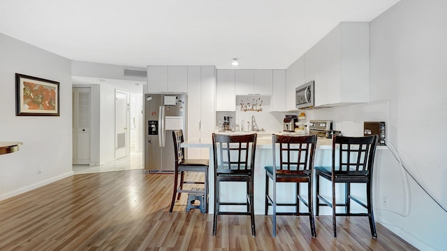 kitchen featuring sink, a breakfast bar area, white cabinets, stainless steel appliances, and light hardwood / wood-style flooring