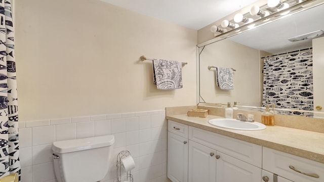 bathroom featuring vanity, tile walls, and toilet