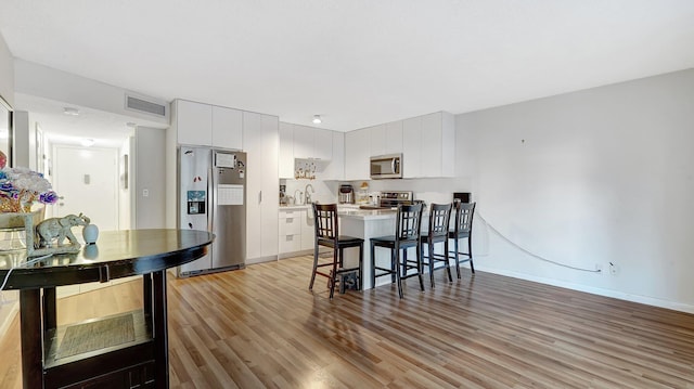 kitchen with stainless steel appliances, a breakfast bar area, white cabinets, and light hardwood / wood-style flooring