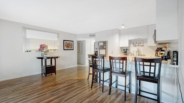 kitchen with sink, a breakfast bar, appliances with stainless steel finishes, wood-type flooring, and white cabinets