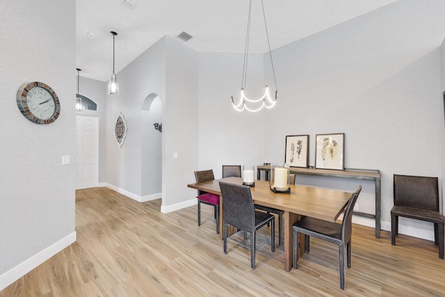 dining space featuring a chandelier, high vaulted ceiling, and light hardwood / wood-style flooring