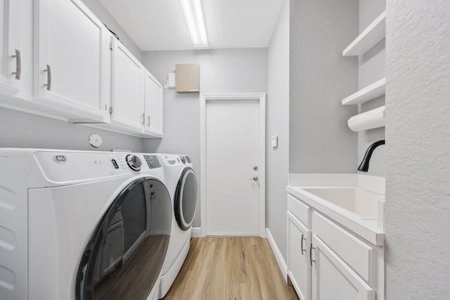 laundry room featuring sink, cabinets, a textured ceiling, washer and clothes dryer, and light hardwood / wood-style floors