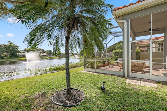 view of yard featuring a water view, ceiling fan, and glass enclosure