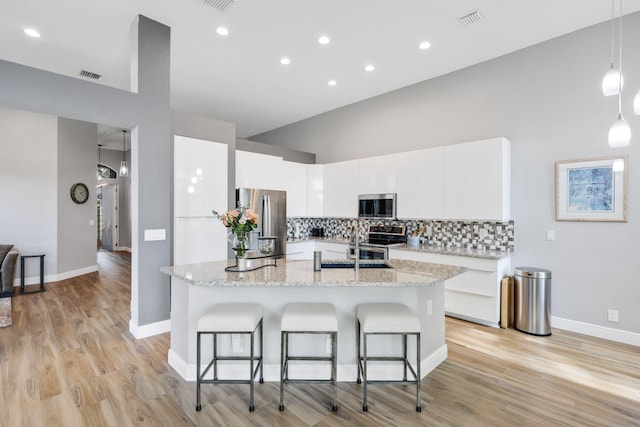 kitchen with pendant lighting, a breakfast bar area, stainless steel appliances, white cabinets, and decorative backsplash