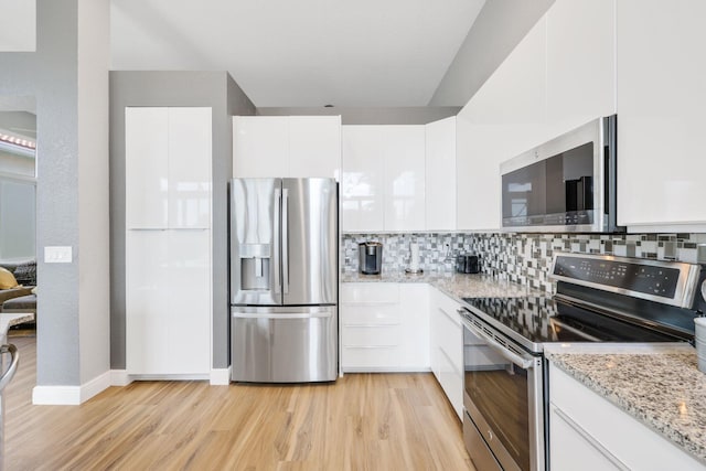 kitchen featuring appliances with stainless steel finishes, tasteful backsplash, white cabinets, light stone countertops, and light wood-type flooring