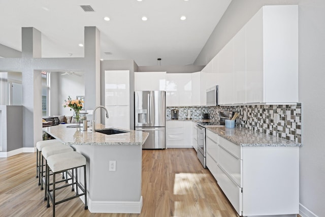 kitchen with sink, backsplash, stainless steel appliances, white cabinets, and light wood-type flooring