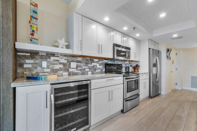 kitchen featuring wine cooler, appliances with stainless steel finishes, a tray ceiling, decorative backsplash, and white cabinets