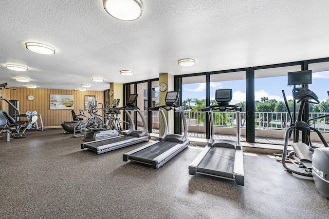 workout area featuring wood walls, a textured ceiling, and a wall of windows