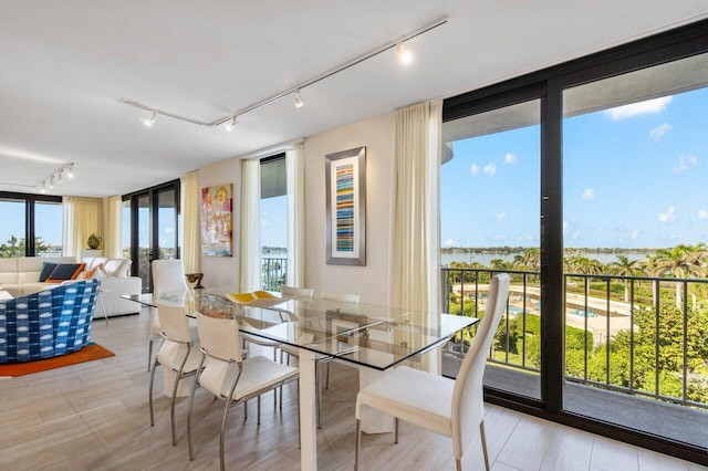 dining space with a water view, floor to ceiling windows, rail lighting, and light wood-type flooring