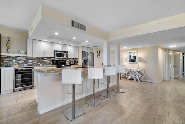 kitchen with a kitchen breakfast bar, stainless steel appliances, light stone counters, a center island with sink, and beverage cooler