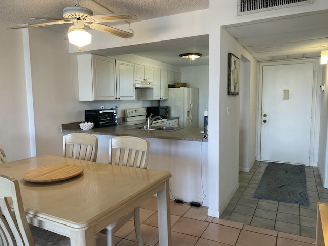 kitchen featuring light tile patterned flooring, white refrigerator with ice dispenser, ceiling fan, kitchen peninsula, and a textured ceiling