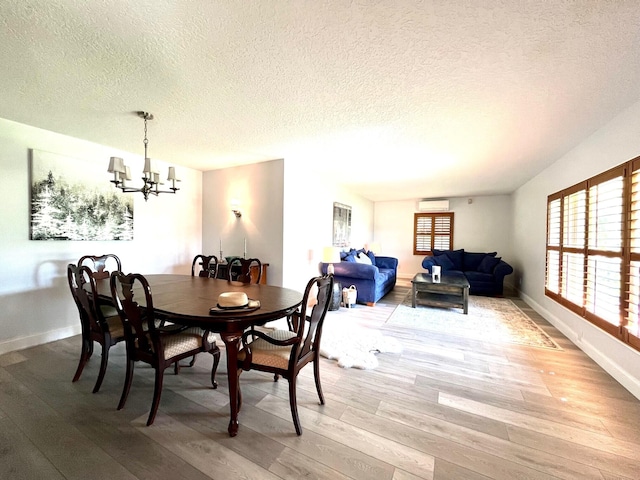 dining room with a wall mounted AC, a textured ceiling, a chandelier, and light hardwood / wood-style floors