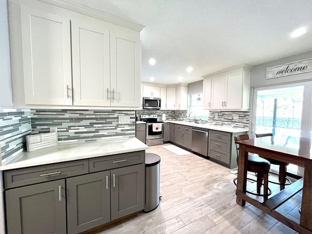 kitchen featuring appliances with stainless steel finishes, gray cabinetry, backsplash, light hardwood / wood-style floors, and white cabinets