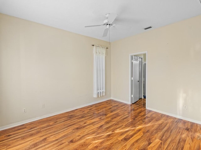 empty room with wood finished floors, a ceiling fan, and baseboards