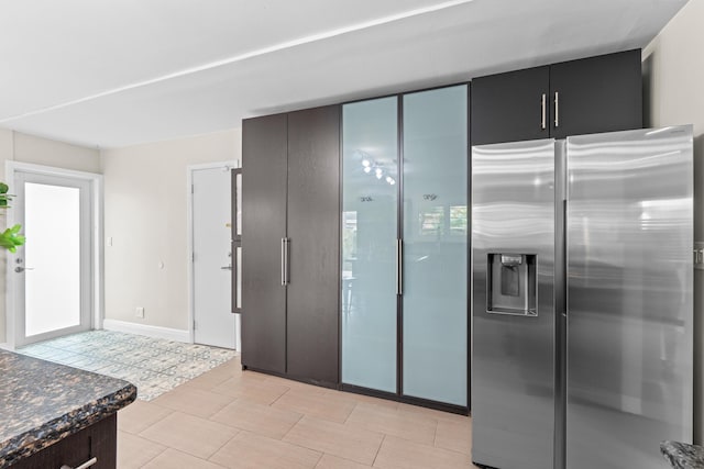 kitchen with stainless steel refrigerator with ice dispenser, light tile patterned floors, and dark stone counters