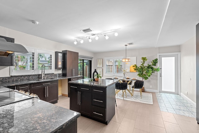 kitchen featuring sink, hanging light fixtures, a center island, extractor fan, and dark stone counters