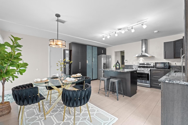 kitchen featuring hanging light fixtures, appliances with stainless steel finishes, dark stone countertops, and wall chimney exhaust hood