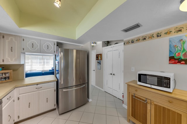 kitchen with a tray ceiling, stainless steel fridge, white cabinets, and light tile patterned flooring