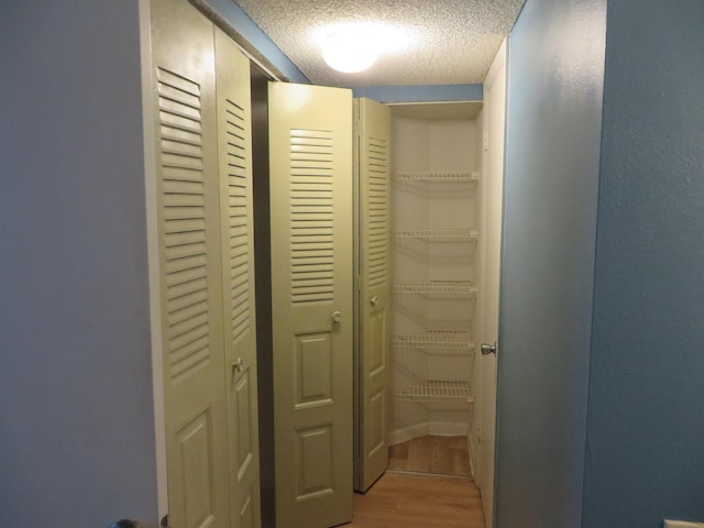 corridor with a textured ceiling and light hardwood / wood-style floors