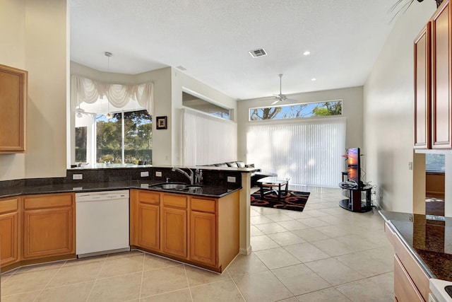 kitchen featuring sink, light tile patterned floors, dishwasher, dark stone countertops, and hanging light fixtures