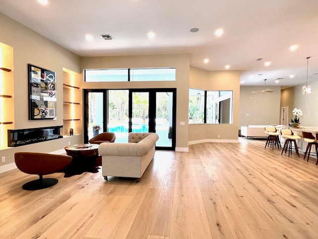 living room featuring light wood finished floors, baseboards, visible vents, built in shelves, and recessed lighting