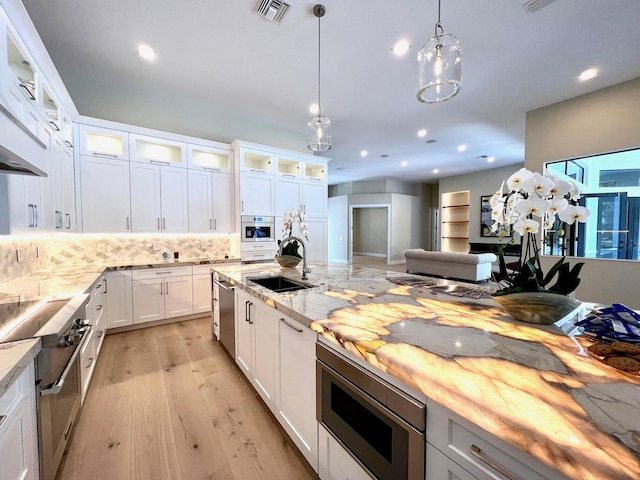 kitchen featuring stainless steel appliances, a sink, visible vents, hanging light fixtures, and light wood-type flooring