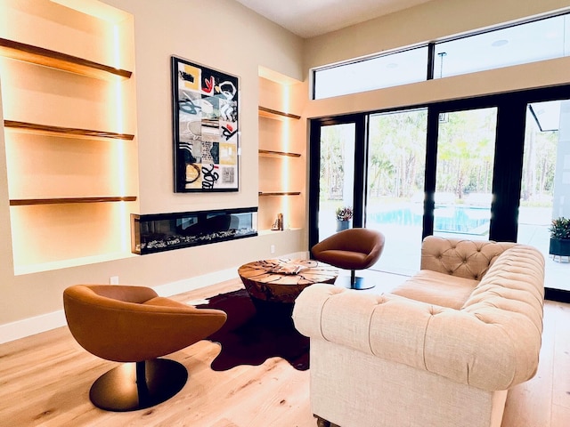 home theater featuring built in shelves, baseboards, wood finished floors, and a glass covered fireplace