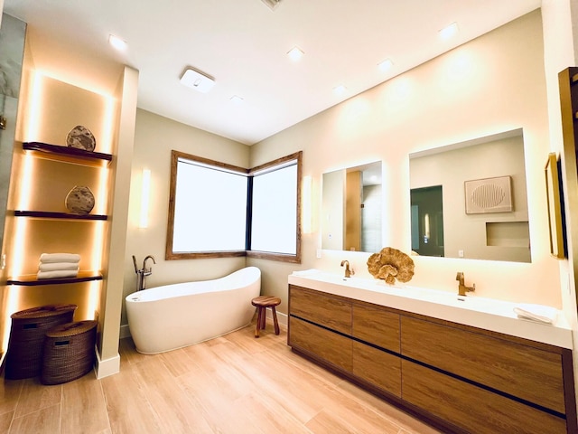 bathroom featuring double vanity, a sink, wood finished floors, a freestanding tub, and baseboards