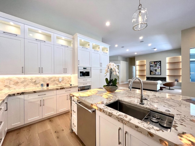 kitchen with decorative backsplash, white cabinets, appliances with stainless steel finishes, light wood-style floors, and a sink