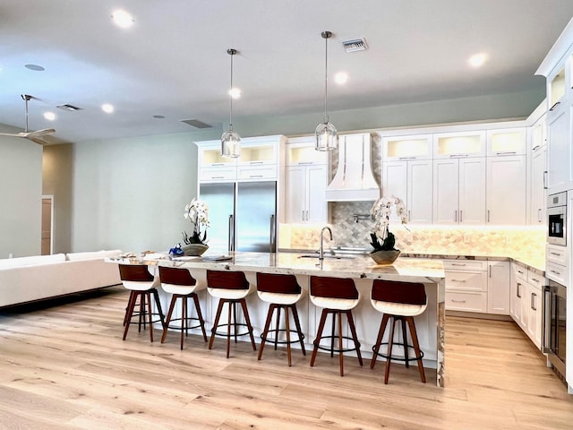 kitchen with built in fridge, light wood-style floors, a large island, and decorative backsplash