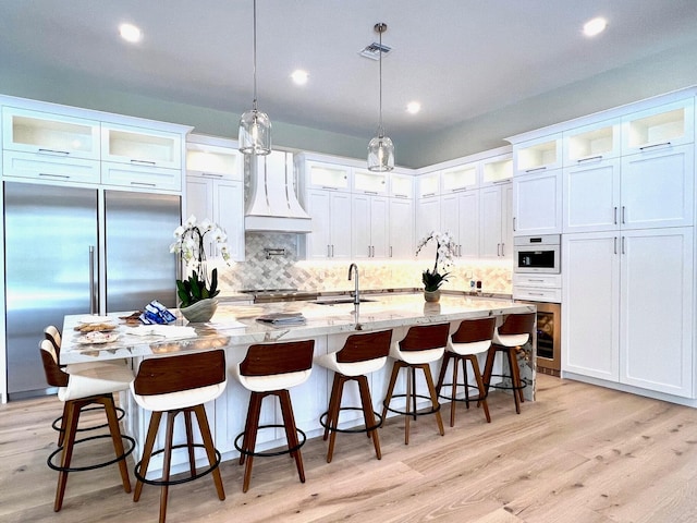 kitchen featuring light wood-style floors, white cabinets, stainless steel built in fridge, a sink, and premium range hood