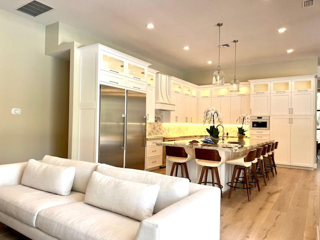 kitchen with visible vents, open floor plan, white oven, stainless steel built in fridge, and a kitchen bar