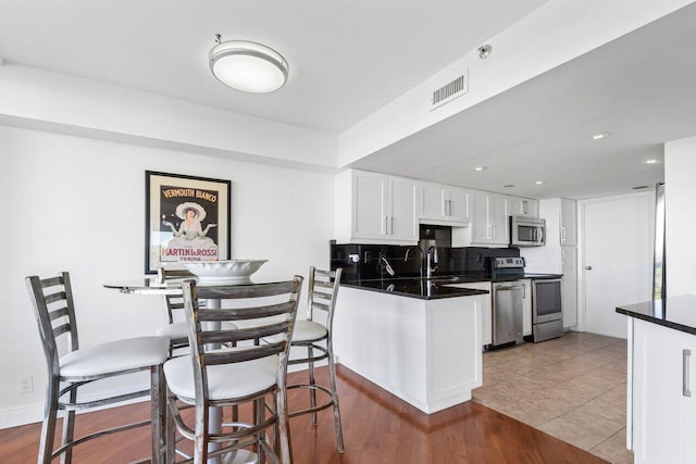 kitchen featuring white cabinetry, kitchen peninsula, stainless steel appliances, tile patterned flooring, and backsplash