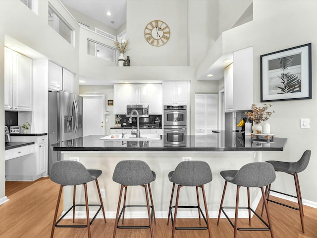 kitchen featuring white cabinetry, light hardwood / wood-style flooring, appliances with stainless steel finishes, kitchen peninsula, and a high ceiling