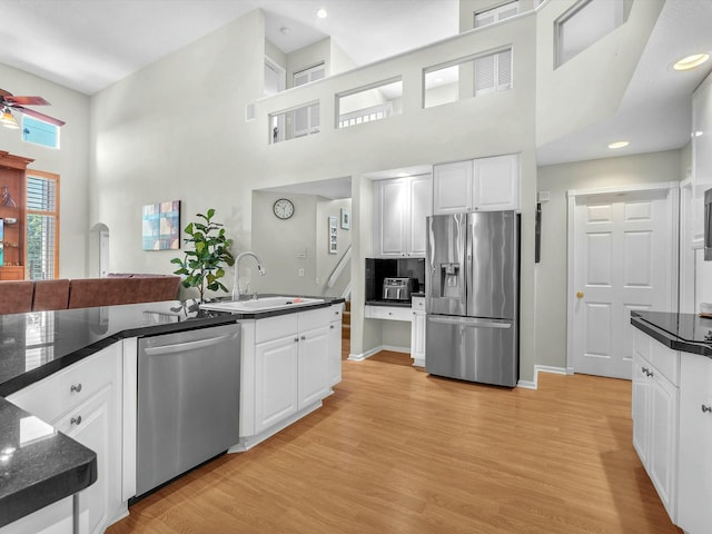 kitchen featuring white cabinetry, light wood-type flooring, a high ceiling, and appliances with stainless steel finishes